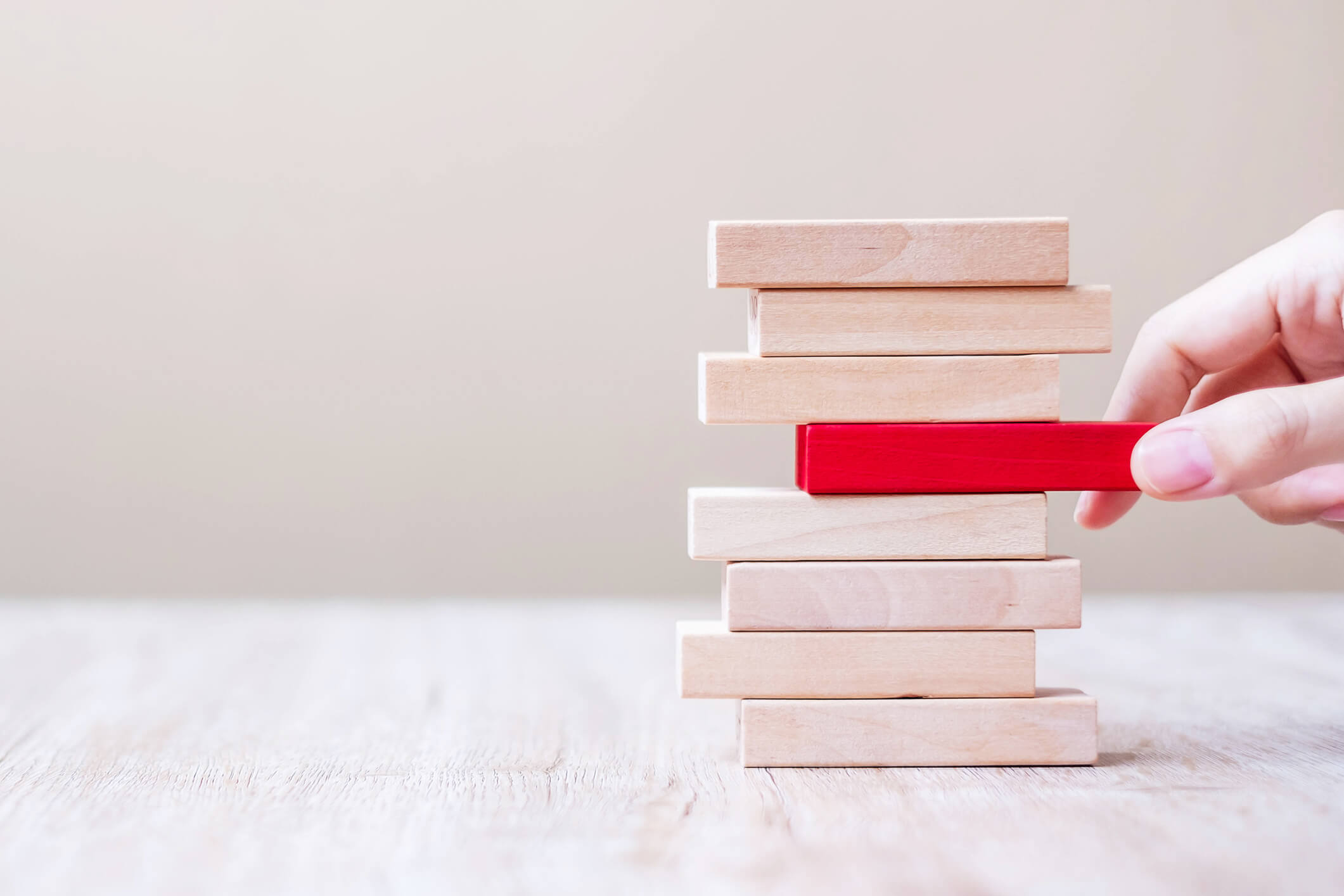 tower of wooden blocks with red block being pulled out of the middle to demonstrate risk management