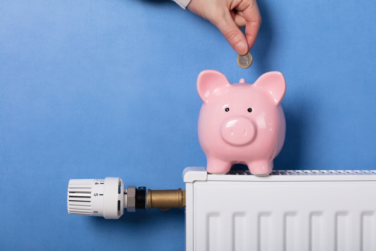 person putting money in piggy bank on top of radiator to show energy bill concept