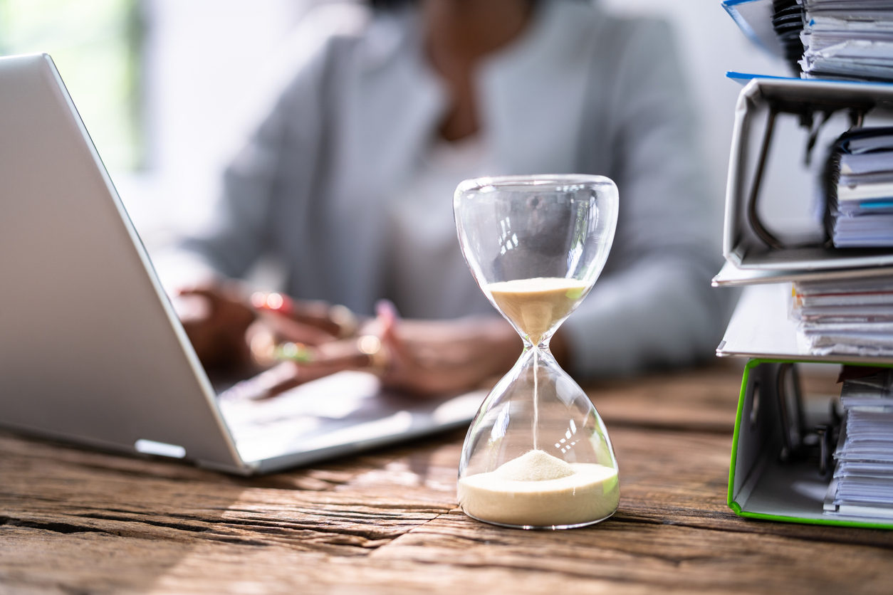 business woman on laptop with sand timer in front to represent waiting for payment